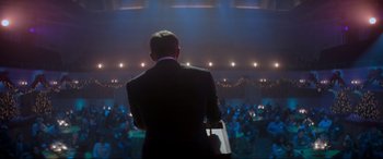 Movie still from “Spirited” (2022), directed by Sean Anders – A man standing in front of an audience in a dark room; Medium shot, Over the shoulder angle