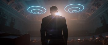 Movie still from “Spirited” (2022), directed by Sean Anders – A man in a suit standing in front of lights; Medium shot, Low angle