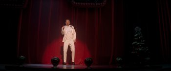 Movie still from “Spirited” (2022), directed by Sean Anders – A man standing on a stage wearing a white suit; Wide shot, Low angle