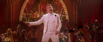 Movie still from “Spirited” (2022), directed by Sean Anders – A man in a white suit is singing; Medium shot, Low angle