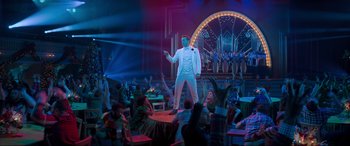 Movie still from “Spirited” (2022), directed by Sean Anders – A wax statue of a man in a white suit is on display in front of a group of people; Wide shot, High angle