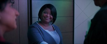 Movie still from “Spirited” (2022), directed by Sean Anders – A woman smiling for the camera in front of a wall; Medium shot, Over the shoulder angle