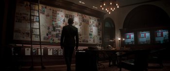 Movie still from “Spirited” (2022), directed by Sean Anders – A man standing in front of a wall covered in pictures; Wide shot, Over the shoulder angle