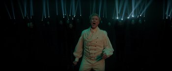 Movie still from “Spirited” (2022), directed by Sean Anders – A group of people in a room with a man in a white suit; Medium shot, Low angle