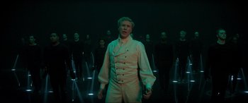 Movie still from “Spirited” (2022), directed by Sean Anders – A group of people standing in front of a man in white; Medium shot, High angle