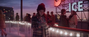 Movie still from “Spirited” (2022), directed by Sean Anders – A woman in a plaid coat and a red hat looking at her cell phone; Medium shot, Low angle