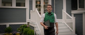 Movie still from “Spirited” (2022), directed by Sean Anders – A man holding a laptop standing in front of a house; Medium shot, Low angle
