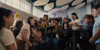 Movie still from “Spy Kids: Armageddon” (2023), directed by Robert Rodriguez – A group of people gathered around a young boy holding a tablet; Wide shot, High angle