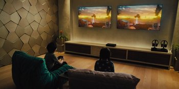 Movie still from “Spy Kids: Armageddon” (2023), directed by Robert Rodriguez – Two people sitting in front of a television in a living room; Wide shot, High angle