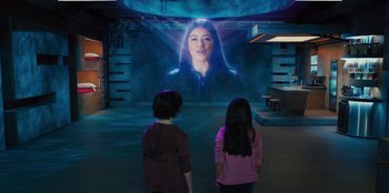 Movie still from “Spy Kids: Armageddon” (2023), directed by Robert Rodriguez – Two young children standing in front of a projected image of a woman; Medium shot, Over the shoulder angle