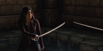 Movie still from “Spy Kids: Armageddon” (2023), directed by Robert Rodriguez – A woman holding a sword in front of a brick wall; Medium shot, Over the shoulder angle