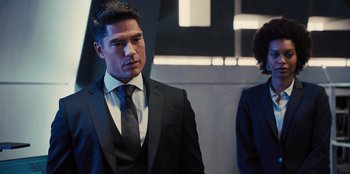 Movie still from “Spy Kids: Armageddon” (2023), directed by Robert Rodriguez – A man in a suit and tie standing next to another man in a suit and tie; Medium shot, Over the shoulder angle