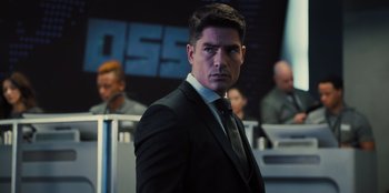 Movie still from “Spy Kids: Armageddon” (2023), directed by Robert Rodriguez – A man in a suit and tie standing in front of other men; Close Up shot, Over the shoulder angle