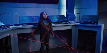 Movie still from “Spy Kids: Armageddon” (2023), directed by Robert Rodriguez – A young girl standing in a room with lasers in front of a desk; Medium shot, High angle