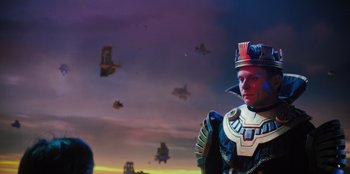 Movie still from “Spy Kids: Armageddon” (2023), directed by Robert Rodriguez – A man wearing a crown and a suit of armor standing in front of a sky filled with flying vehicles; Medium shot, Low angle