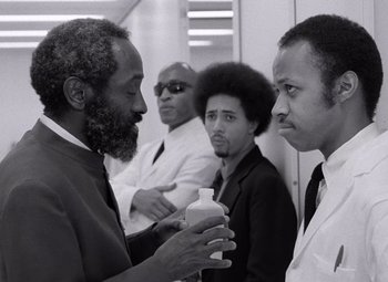 A black and white photo of two men talking to each other
