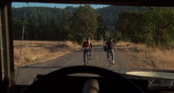 Movie still from “Stand by Me” (1986), directed by Rob Reiner – Two people riding bikes down a dirt road near a forest; Wide shot, Low angle