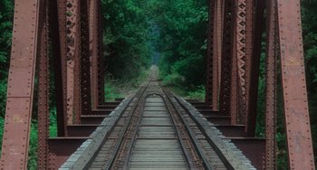 Movie still from “Stand by Me” (1986), directed by Rob Reiner – A train track going under a bridge with trees in the background; Extreme Wide shot, High angle