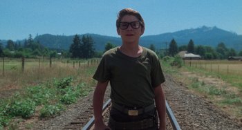 Movie still from “Stand by Me” (1986), directed by Rob Reiner – A young man wearing glasses standing on a train track; Medium shot, Low angle