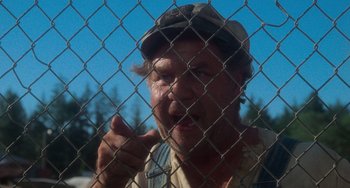 Movie still from “Stand by Me” (1986), directed by Rob Reiner – A man in a cap is standing behind a chain link fence; Close Up shot, Over the shoulder angle