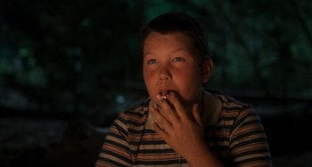 Movie still from “Stand by Me” (1986), directed by Rob Reiner – A young boy sitting in front of a tree eating a piece of food; Close Up shot, Low angle