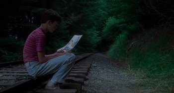 Movie still from “Stand by Me” (1986), directed by Rob Reiner – A man sitting on the side of a train track; Medium shot, High angle