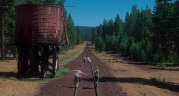 Movie still from “Stand by Me” (1986), directed by Rob Reiner – Three men are standing on a train track near a water tower; Extreme Wide shot, High angle
