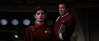 Movie still from “Star Trek II: The Wrath of Khan” (1982), directed by Nicholas Meyer – A man and a woman dressed in red are posing for a picture; Medium shot, Low angle