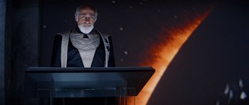 Movie still from “Star Trek IV: The Voyage Home” (1986), directed by Leonard Nimoy – An old man wearing a suit and tie standing at a podium in front of an image of the moon; Medium shot, Over the shoulder angle
