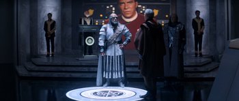 Movie still from “Star Trek IV: The Voyage Home” (1986), directed by Leonard Nimoy – A man dressed as a klingon standing in front of an image of a klingon; Wide shot, Over the shoulder angle
