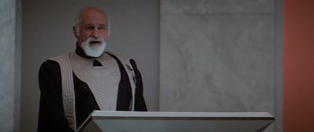 Movie still from “Star Trek IV: The Voyage Home” (1986), directed by Leonard Nimoy – An older man in a suit and tie standing in front of a podium; Medium shot, Low angle