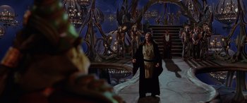 Movie still from “Star Wars: Episode I - The Phantom Menace” (1999), directed by George Lucas – A man dressed as obi - wan kenobi stands in front of a mural; Extreme Wide shot, High angle