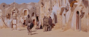 Movie still from “Star Wars: Episode I - The Phantom Menace” (1999), directed by George Lucas – A group of people standing in the sand near a building; Wide shot, High angle