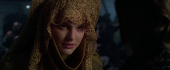 Movie still from “Star Wars: Episode II - Attack of the Clones” (2002), directed by George Lucas – A young woman wearing a gold headdress and a yellow dress; Close Up shot, Over the shoulder angle