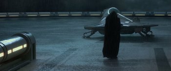 Movie still from “Star Wars: Episode II - Attack of the Clones” (2002), directed by George Lucas – A person in a hooded cloak standing next to a bench in the dark; Extreme Wide shot, Over the shoulder angle