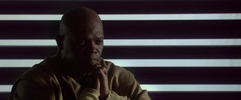Movie still from “Star Wars: Episode II - Attack of the Clones” (2002), directed by George Lucas – A man sitting in front of a striped wall with his hands under his chin; Close Up shot, Low angle