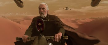 Movie still from “Star Wars: Episode II - Attack of the Clones” (2002), directed by George Lucas – An older man riding a motorcycle in a desert; Medium shot, Over the shoulder angle
