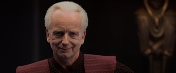 Movie still from “Star Wars: Episode III - Revenge of the Sith” (2005), directed by George Lucas – An older man with white hair wearing a red and black shirt; Close Up shot, Over the shoulder angle