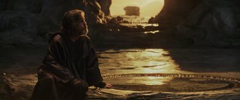 Movie still from “Star Wars: Episode VIII - The Last Jedi” (2017), directed by Rian Johnson – A man sitting on the ground near a body of water; Wide shot, Over the shoulder angle