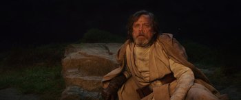 Movie still from “Star Wars: Episode VIII - The Last Jedi” (2017), directed by Rian Johnson – A man with a beard is sitting on some rocks; Medium shot, Low angle