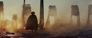 Movie still from “Star Wars: Episode VIII - The Last Jedi” (2017), directed by Rian Johnson – A man in a black cape walking in front of a pair of star wars vehicles; Wide shot, Low angle