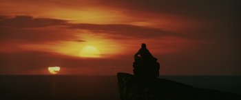 Movie still from “Star Wars: Episode VIII - The Last Jedi” (2017), directed by Rian Johnson – A man sitting on top of a rock looking at the sunset; Extreme Wide shot, Low angle