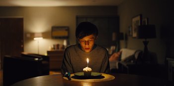 Movie still from “Stargirl” (2020), directed by Julia Hart – A young boy sitting in front of a lit birthday candle; Medium shot, High angle