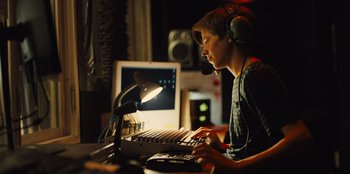 Movie still from “Stargirl” (2020), directed by Julia Hart – A man wearing headphones and using a computer keyboard; Medium shot, Low angle
