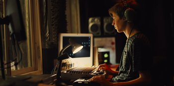 Movie still from “Stargirl” (2020), directed by Julia Hart – A man sitting in front of a computer keyboard; Medium shot, Low angle