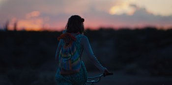Movie still from “Stargirl” (2020), directed by Julia Hart – A person riding a bike with a backpack; Medium shot, Over the shoulder angle