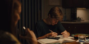 Movie still from “Stargirl” (2020), directed by Julia Hart – A young boy is writing on a book; Medium shot, Over the shoulder angle