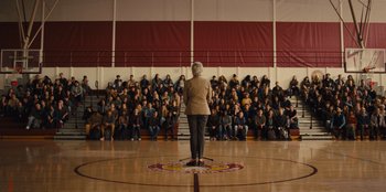 Movie still from “Stargirl” (2020), directed by Julia Hart – An older woman standing in front of a crowd of people in a gym; Extreme Wide shot, High angle