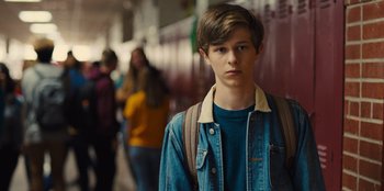 Movie still from “Stargirl” (2020), directed by Julia Hart – A boy with a backpack standing in front of a wall of lockers; Medium shot, Over the shoulder angle