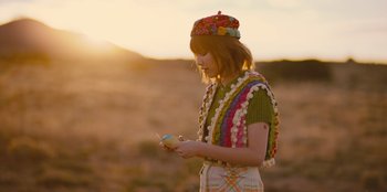 Movie still from “Stargirl” (2020), directed by Julia Hart – A woman wearing a hat and holding a cell phone in her hand; Medium shot, Over the shoulder angle